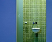 View of designer wash basin on wall with green mosaic tiles through open door