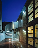 Zeitgenössisches Wohnhaus im Dämmerlicht - Stahlwendeltreppe und nasser Holzbelag in beleuchtetem Innenhof