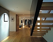 Schwebende Treppe zwischen Wand und dunkler Wangenscheibe in breitem Flur mit Blick in offenen Wohnraum