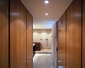 View between wall units to wooden bathtub and shower area with wooden slatted floor in modern ensuite bathroom
