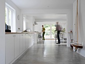 Woman in front of long kitchen unit and man in dining area of modern room with concrete floor