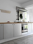 Modern, white kitchen units with wooden work surface, stainless steel oven, hob and extractor fan and concrete floor