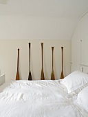 Double bed with snow-white covers and old boat paddles as decoration in traditional attic bedroom