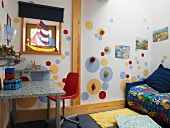 Colourful child's bedroom with sailing boat in window and slanting light from above falling on circles of colour with climbing holds