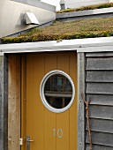 Front door with bulls-eye window beneath slanting turf roof