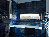 Bathroom with view of landscape through narrow, horizontal window and bold, mottled blue tiles