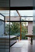 Modern bathroom in solar house with view of sky and trees through glass wall with sliding element and glass roof