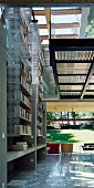 Zweigeschossige Bücherwand zwischen Betonscheiben und Schieberegale aus Lochblechkonstruktion in Wohnraum mit Galerie-Ebene