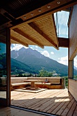 Sunny, partially roofed wooden terrace with generous corner bench and view of mountains