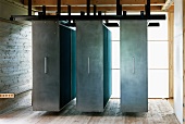 Suspended, moveable cupboards with steel doors in front of translucent walls in contemporary house