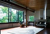 Offener Wohnraum in modernem Holzhaus mit Wand- und Deckenpaneelen, grossen Schiebefenstern und skulpturalem Kamin