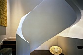 Sculptural spiral staircase with white, masonry balustrade, artwork with text motif and egg-shaped floor lamp