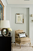 Upholstered armchair with decorative cushions next to chest of drawers and table lamp