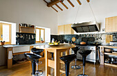 Kitchen island with black bar stools and gas hob with extractor hood