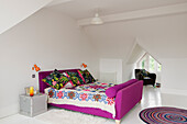 Bedroom with sloping ceiling, purple bed, patterned ceiling and bay window with armchair