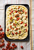 Focaccia topped with tomatoes, olives, capers and cheese on a baking tray