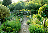 Well-tended garden with symmetrical planting and central path to the bench