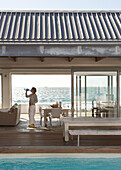 Terrace with pool and dining area by the sea, person drinking water