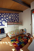 Fröhliches Kinderzimmer unter der Dachschräge mit buntem Teppich im Schachbrettmuster und blauer Tapete mit großen weissen Punkten