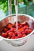 Raspberries and strawberries being washed in a colander