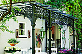 Terrasse mit schmiedeeiserner Pergola und weißen Gartenmöbeln