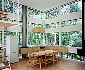 Kitchen with dining area in house made of glass and wood elements in forest
