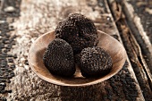 Three black truffles in a wooden bowl on a wooden surface