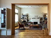 View through wide doorway into modern living room with antique armchairs