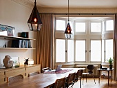 Long wooden table with Bauhaus-era chairs in front of classic bay window
