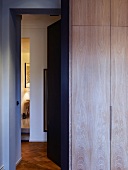 Einbauschrank aus Holz im Schlafraum neben geöffneter Tür mit Blick in Flur