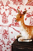 Stuffed fawn on surface in front of wallpaper with erotic pattern