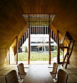 Wooden dining table with rattan chairs in wood-panelled room with view of Japanese courtyard