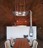 Wooden dining table and rattan chairs in wood-panelled room with white, curved partition