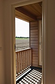 Modernes Holzhaus mit kleinem Balkon - Sonneneinfall durch Geländer und Blick auf Ackerlandschaft
