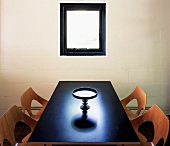Puristischer Raum mit durchbrochenen Schalenstühlen aus Holz und dekorativem Servierteller auf dunklem Tisch