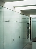 Wall of large, fitted cupboards with white glass doors and bracket handles