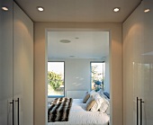 Dressing room with white, glossy fitted wardrobes and open doorway to inviting bedroom