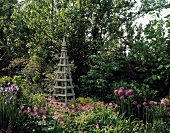 Wooden trellis obelisk in front of trees in cottage garden