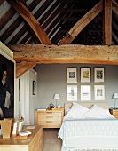 Modernes Schlafzimmer mit hellen Holzmöbeln unter massiven alten Dachbalken