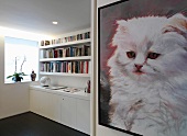 Picture with cat motif on wall of anteroom and bookcase above white sideboard