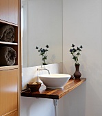 Minimalist washstand with white ceramic basin on wooden counter in corner of bathroom