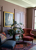 Walls in antique pink, upholstered armchair, table with plant and oriental rug in the living room