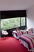 Girl reading comfortably on one of two twin beds with striped covers in designer bedroom