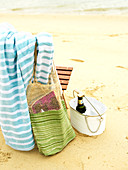 Beach bag and towel hung over chair and drink in metal bucket on sandy ground