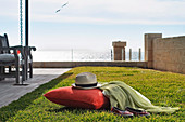 A red pillow and a hat on a lawn with a view of the ocean