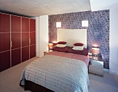 Stacked scatter cushions on bed with upholstered headboard against patterned wallpaper