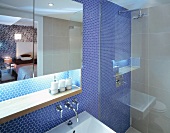 Mirrored cabinet with indirect lighting and shower against wall with blue mosaic tiles