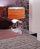 Bedside lamp with transparent, acrylic glass base against patterned wallpaper