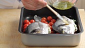 Laying seabream on tomatoes and olives and brushing it with herb oil