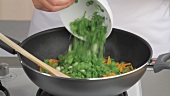 Quickly frying carrots, mangetout and spring onions in a pan
